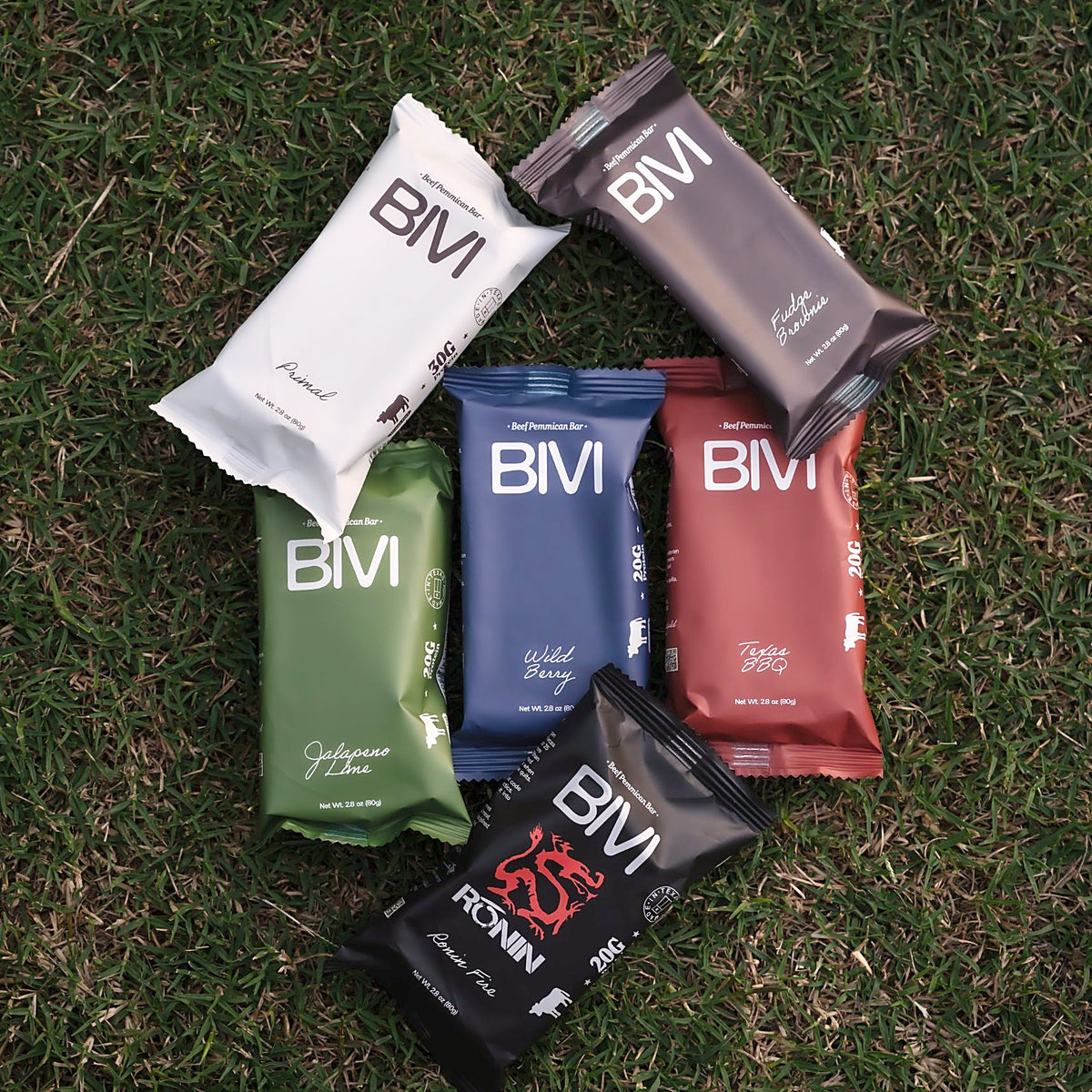 Six BIVI beef pemmican bars, one of each flavor, laid out on grass